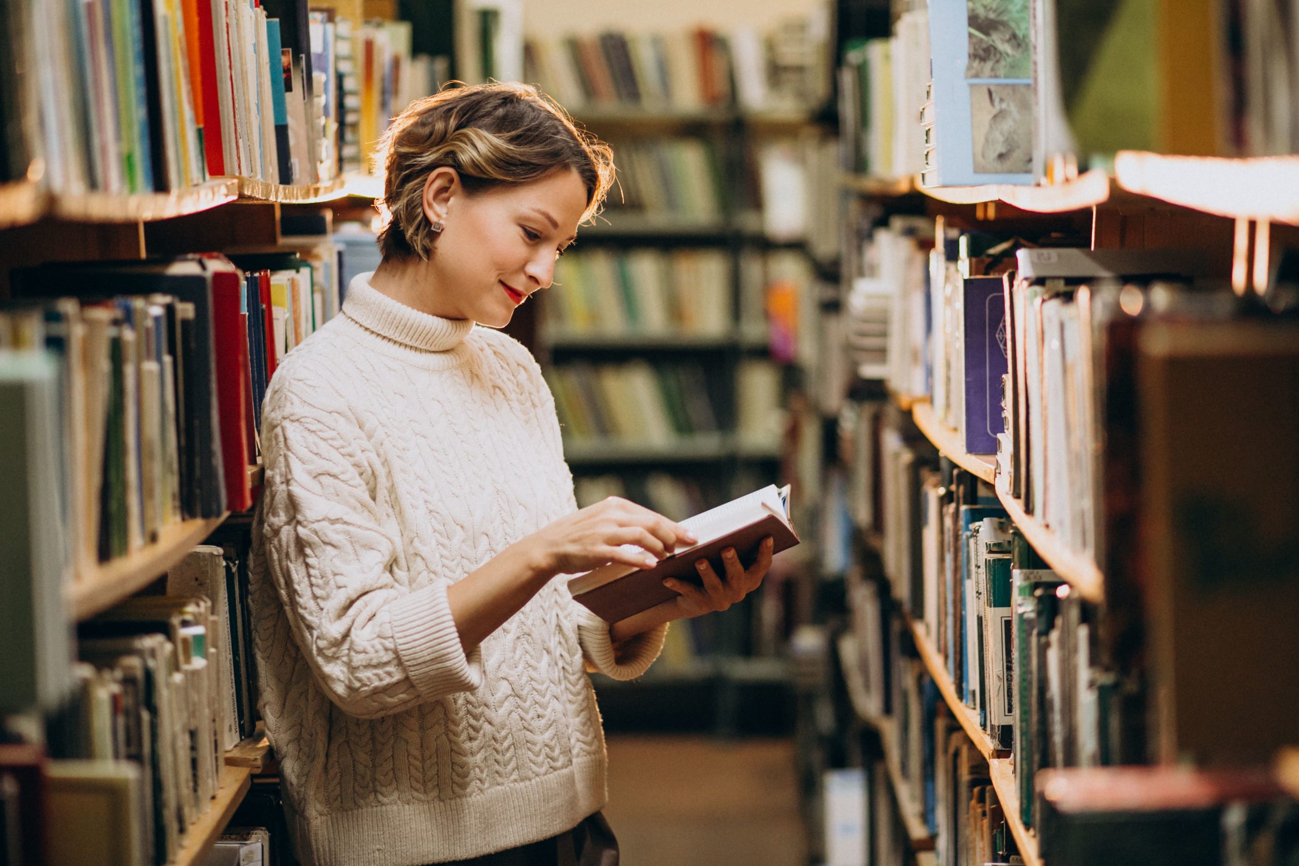 mujer que esta en una biblioteca esta, leyendo un libro en uno de los pasillos de la biblioteca