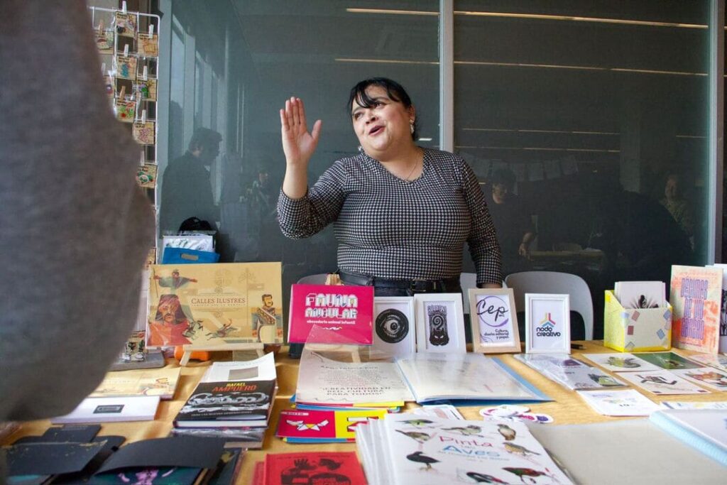 Mujer atendiendo puesto de libros en encuentro editorial A la Vista